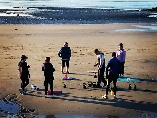 A handful of people with kettlebells and mats training on a beach