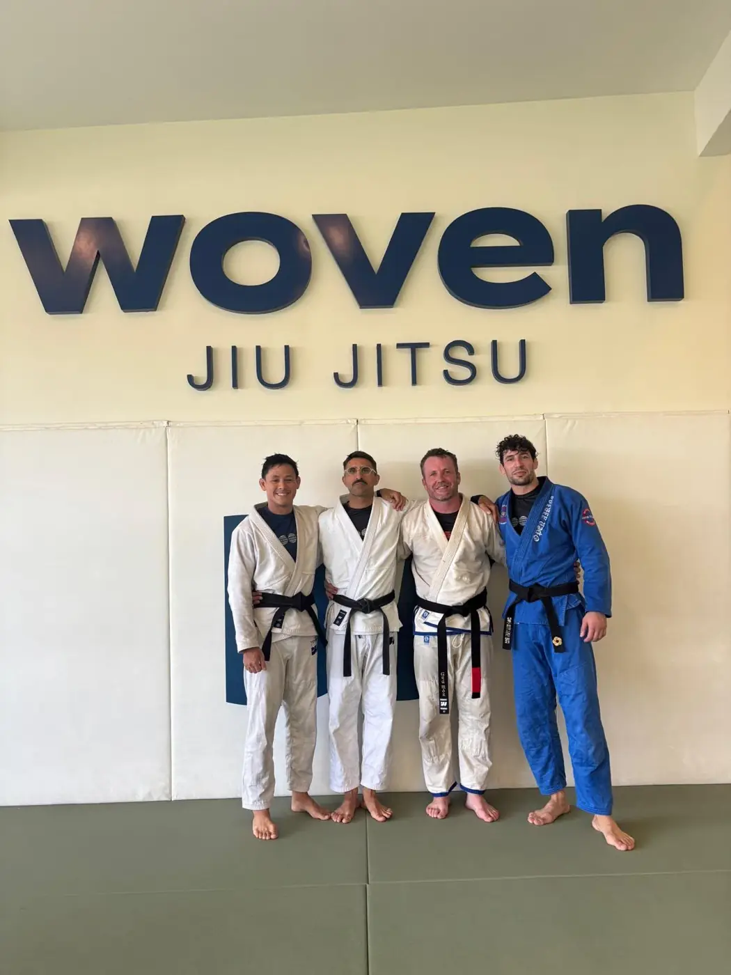 Pat in a white gi and black belt with three training partners on the mats