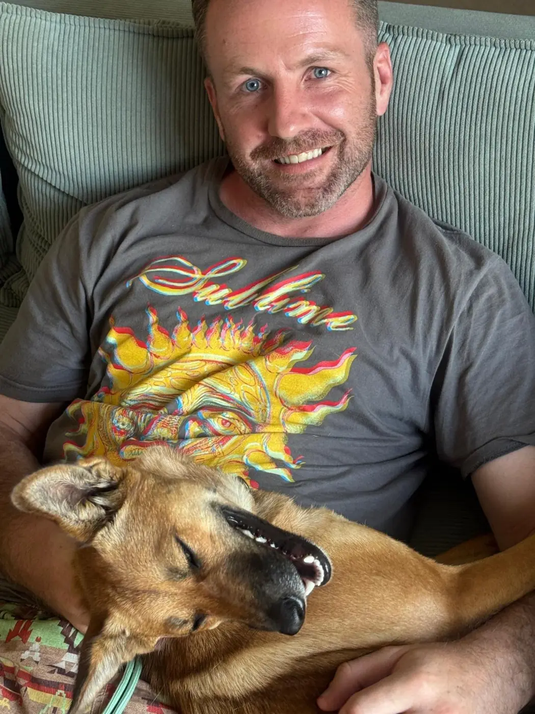 Pat smiling on the sofa with Nova the dog asleep across his lap