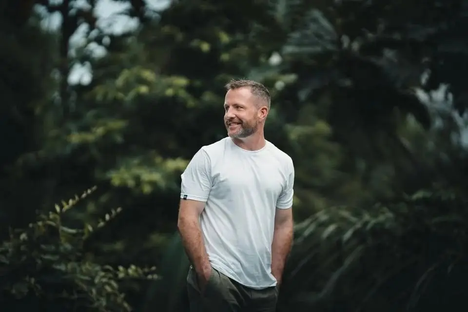 Pat smiling in a white T-shirt among green trees
