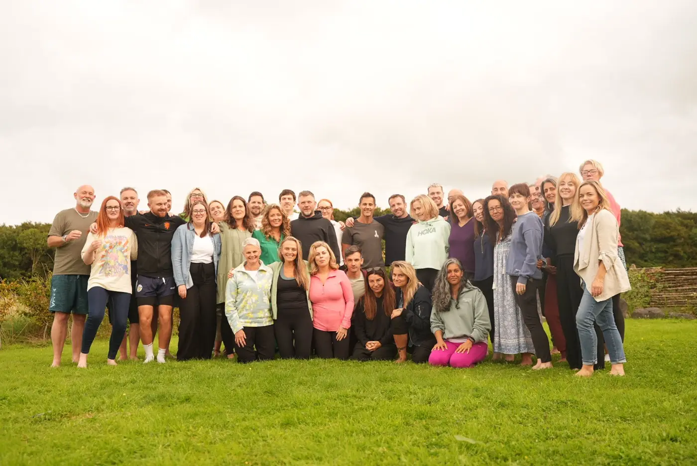 A large group of breathwork trainees standing and kneeling together on a lawn, smiling