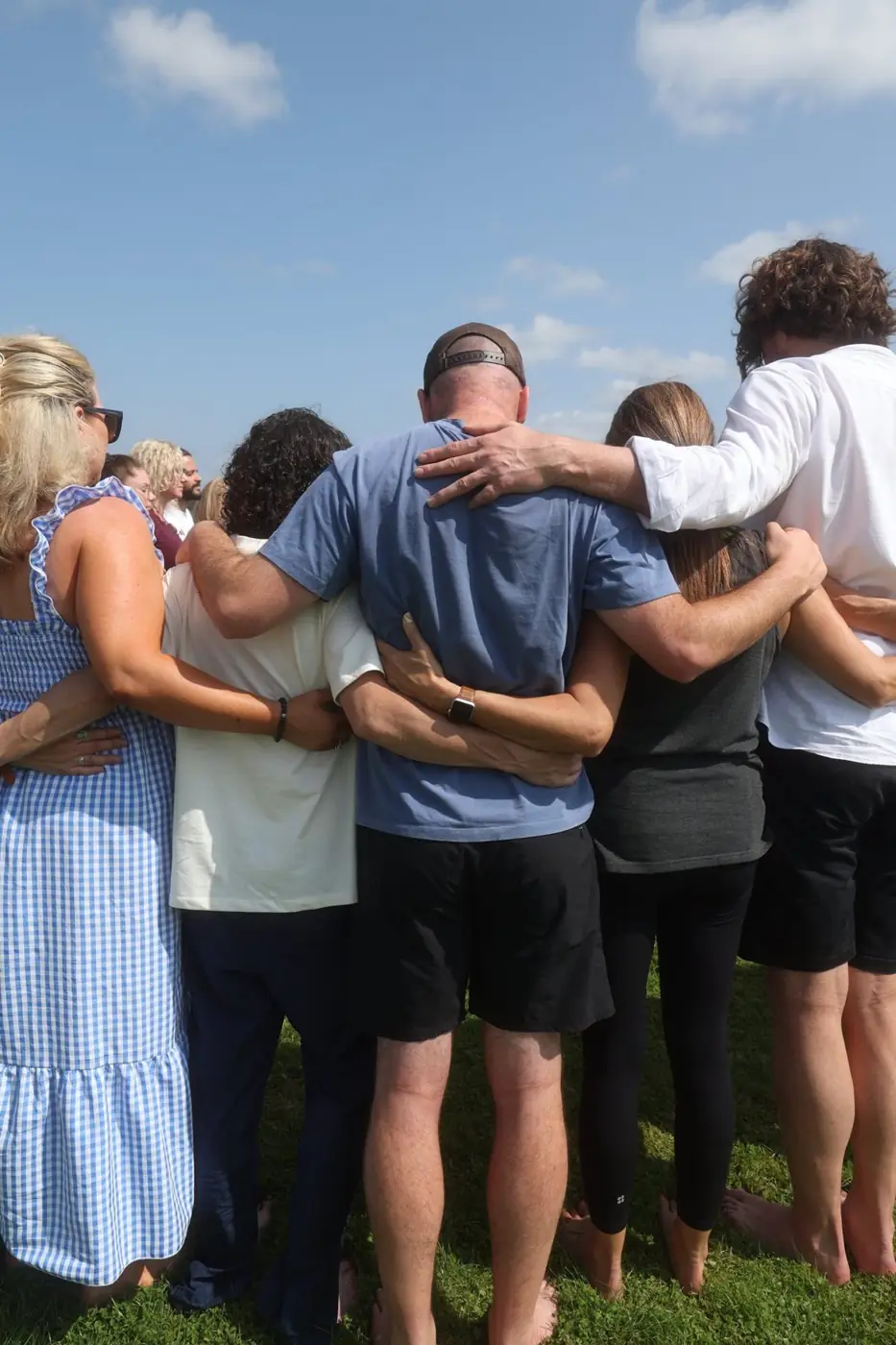 A group of people with their arms around each other on a lawn, seen from behind