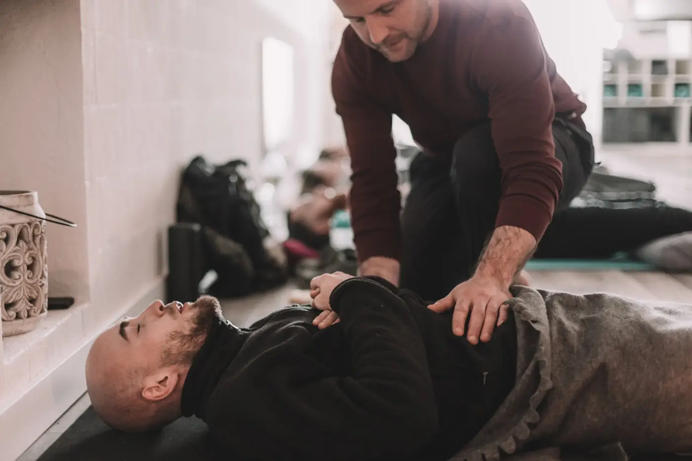 Pat kneeling beside a man lying on a mat, one hand resting on his belly as he breathes