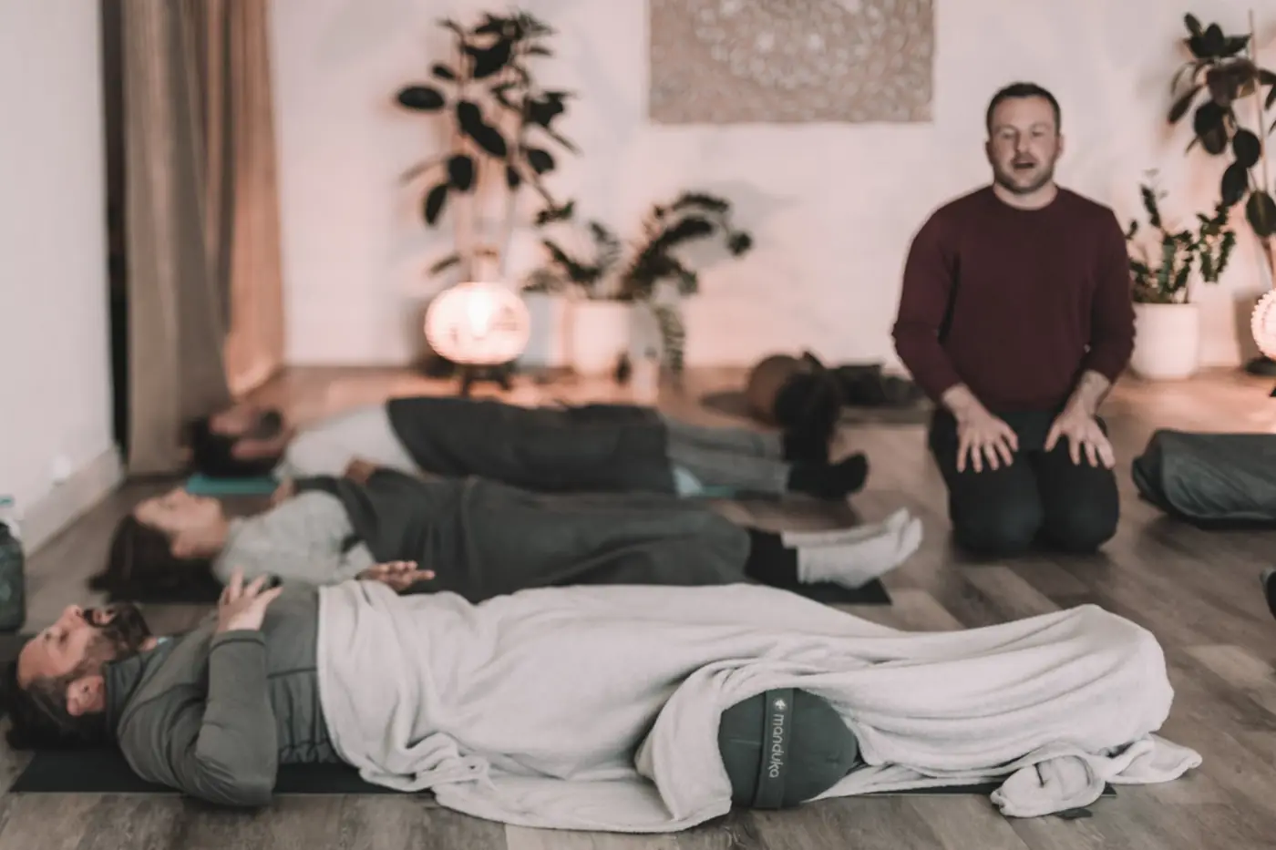 Pat kneeling and guiding a group lying on mats under blankets during a breathwork session