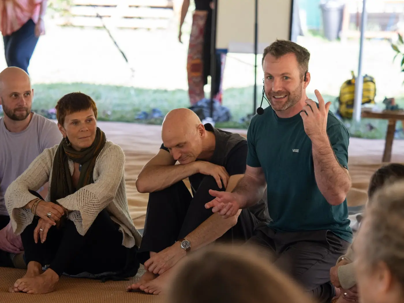 Pat wearing a headset mic, laughing as he teaches a group sitting on the floor of a tent