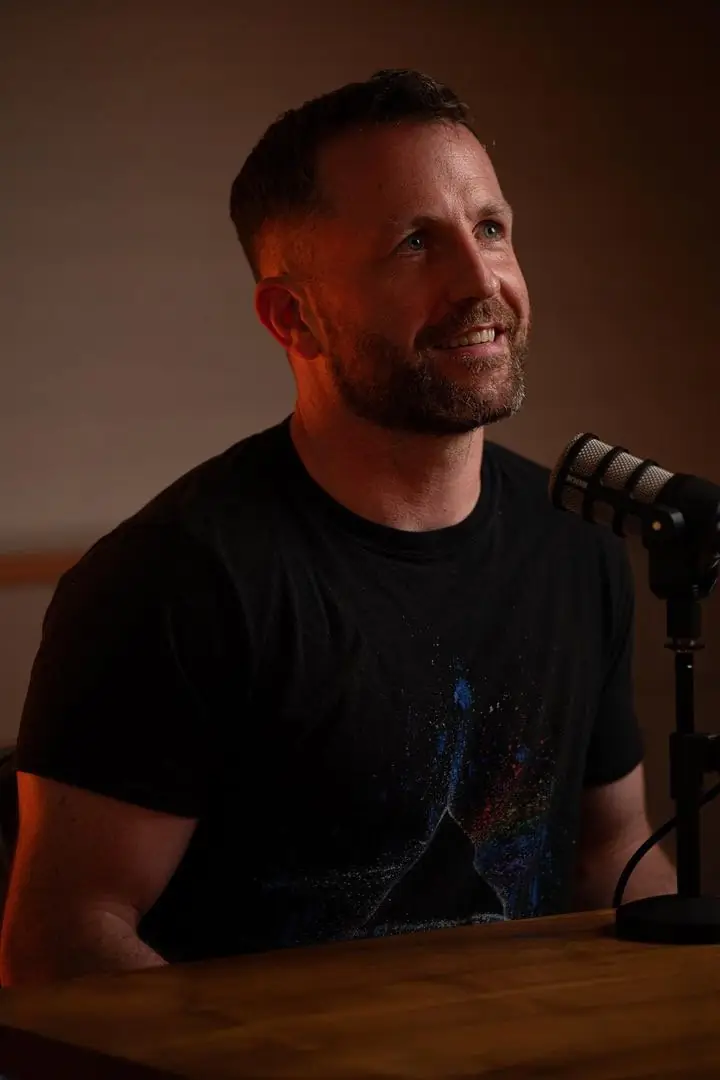 Pat smiling at a microphone in warm low light