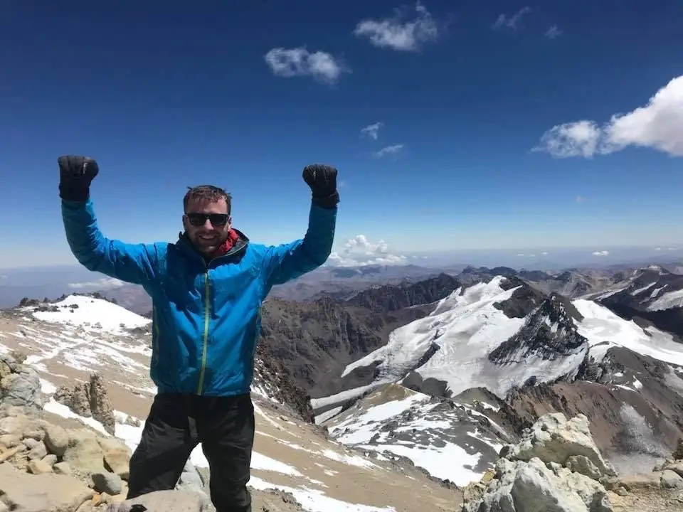 Pat with both arms raised on a high mountain summit