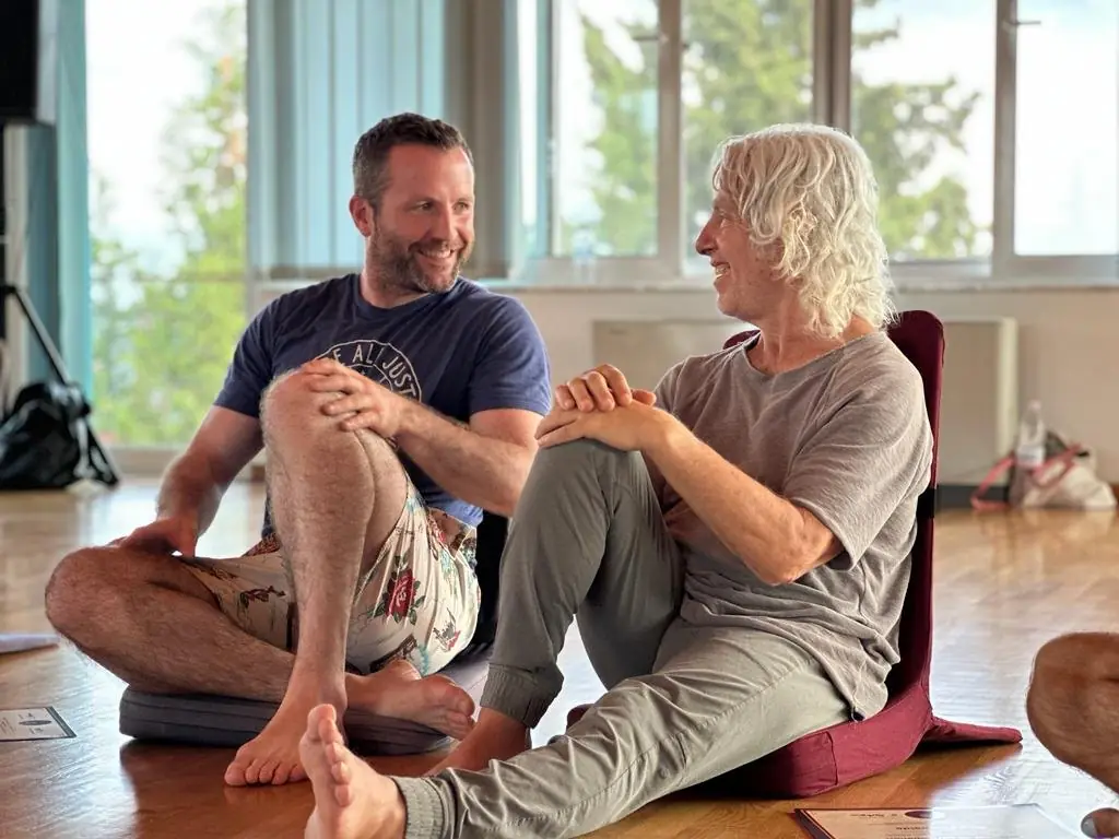 Pat sitting on the floor laughing with a white-haired teacher during a training